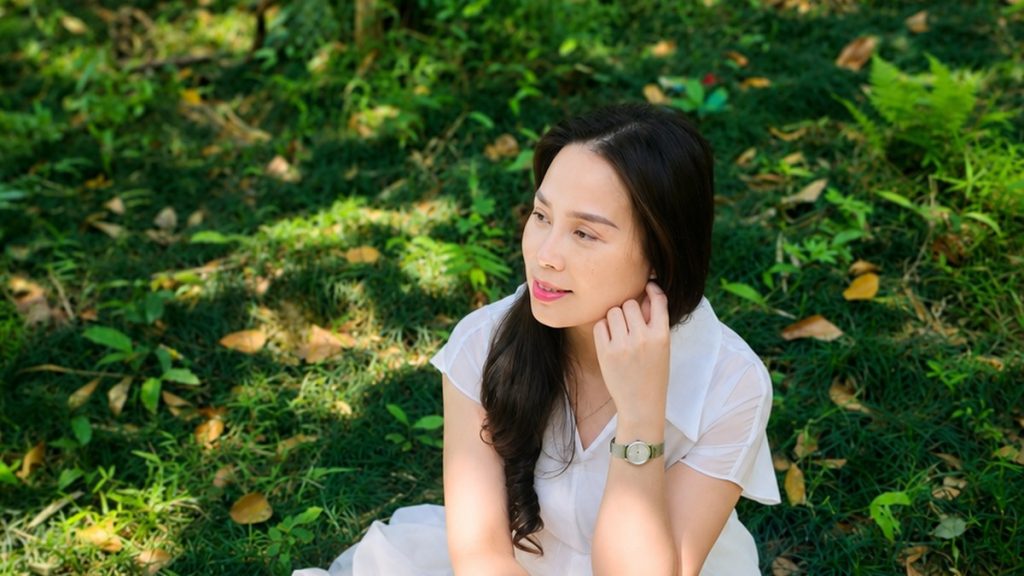 Nhà tâm lý Nguyễn Tú Oanh ngồi trầm ngâm trên nền cỏ, chủ đề dấu hiệu chồng ngoại tình
